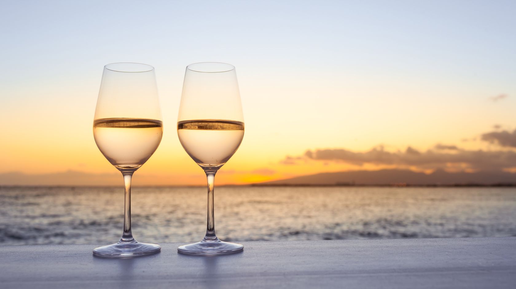 Two glasses of white wine with the Morro Bay sunset as backdrop